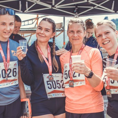 Vier Teilnehmerinnen mit Medaillen stoßen am Verpflegungsstand beim Stolberger Schloss-Lauf mit Wasser an.
